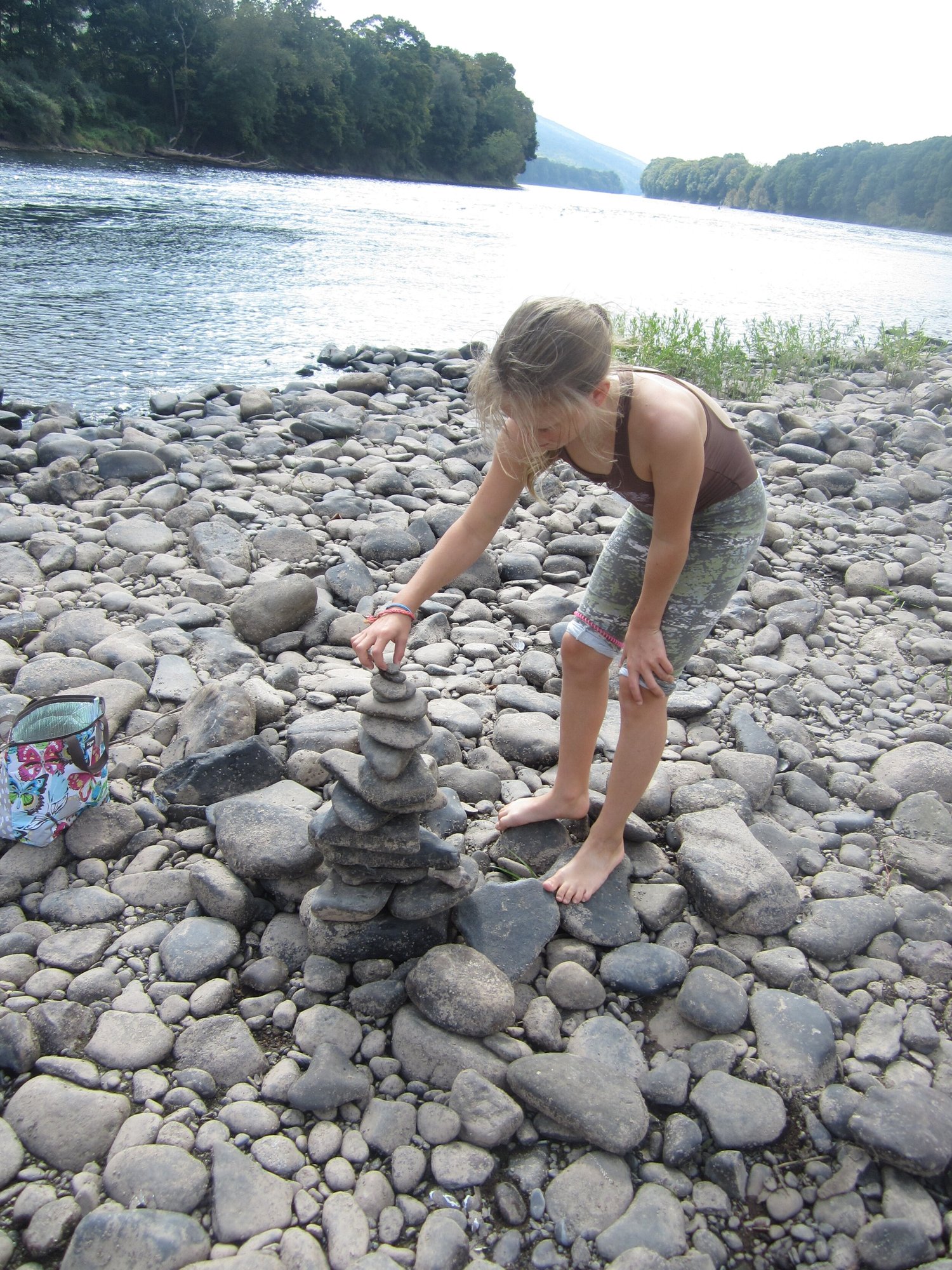 A child balancing stones into a cairn on a riverbank
